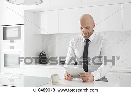 Mid adult businessman using tablet PC in kitchen View Large Photo Image Stock Photo - Mid adult businessman using tablet PC in kitchen. Fotosearch