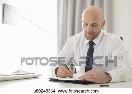 Mid adult businessman writing on clipboard in home office View Large Photo Image Picture - Mid adult businessman writing on clipboard in home office. Fotosearch