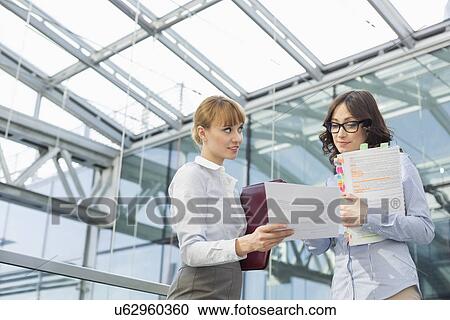Mid-adult businesswoman showing document to female colleague in office View Large Photo Image Stock Image - Mid-adult businesswoman showing document to female colleague in office. Fotosearch