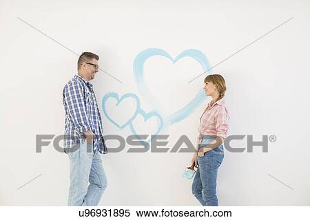Mid-adult couple looking at each other with painted heart on wall View Large Photo Image Stock Photography - Mid-adult couple looking at each other with painted heart on wall. Fotosearch