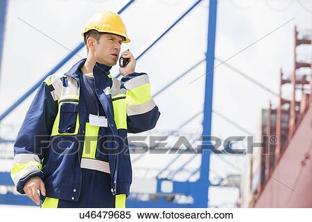 Mid adult male worker using walkie-talkie in shipping yard View Large Photo Image Stock Photography - Mid adult male worker using walkie-talkie in shipping yard. Fotosearch