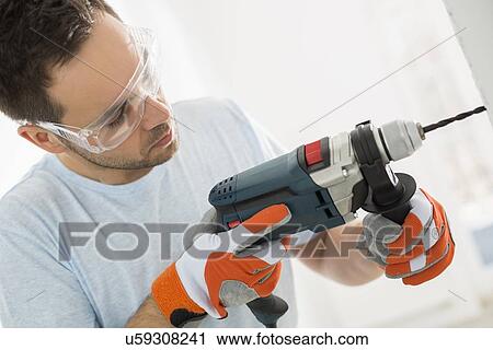 Stock Image - Mid-adult man drilling in wall. Fotosearch