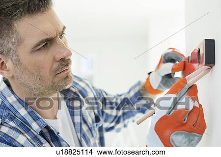 Picture - Mid-adult man marking on wall with level. Fotosearch