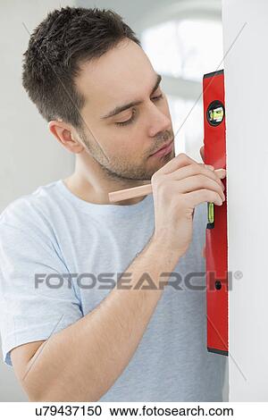 Stock Image - Mid-adult man marking on wall with level. Fotosearch