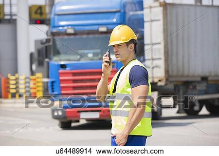 Picture - Mid adult man using walkie-talkie in shipping yard. Fotosearch