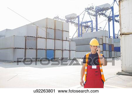 Mid adult man using walkie-talkie in shipping yard View Large Photo Image Stock Image - Mid adult man using walkie-talkie in shipping yard. Fotosearch