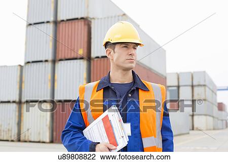 Stock Image - Mid adult man with clipboard in shipping yard. Fotosearch