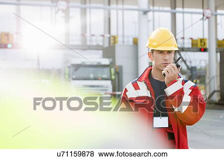 Stock Photo - Mid adult worker using walkie-talkie in shipping yard. Fotosearch