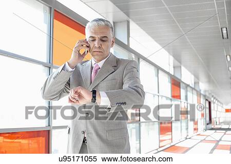 Stock Photography - Middle aged businessman checking time while on call at railroad station. Fotosearch