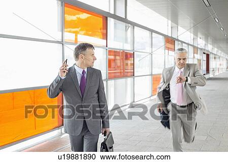 Stock Image - Middle aged businessman looking at colleague running in railroad station. Fotosearch