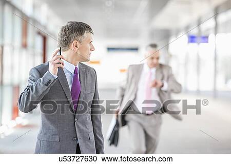 Stock Image - Middle aged businessman looking at colleague running in railroad station. Fotosearch