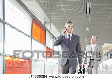 Picture - Middle aged businessman on call while walking in railroad station. Fotosearch