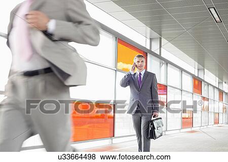 Middle aged businessman on call while walking in railroad station View Large Photo Image Stock Photo - Middle aged businessman on call while walking in railroad station. Fotosearch