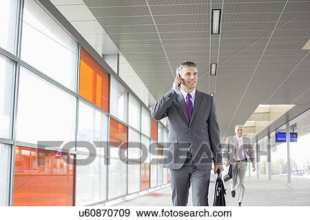 Stock Photo - Middle aged businessman on call while walking in railroad station. Fotosearch