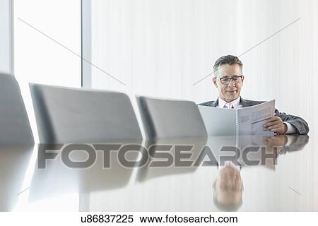 Middle-aged businessman reading book at conference table View Large Photo Image Stock Photography - Middle-aged businessman reading book at conference table. Fotosearch