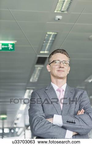 Stock Image - Middle-aged businessman standing with arms crossed in office. Fotosearch