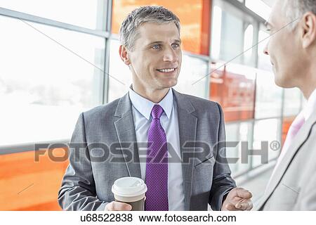 Stock Photo - Middle aged businessman talking with male colleague in railroad station. Fotosearch