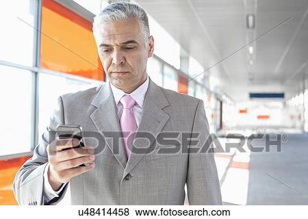 Middle aged businessman text messaging through cell phone at railroad station View Large Photo Image Stock Photo - Middle aged businessman text messaging through cell phone at railroad station. Fotosearch
