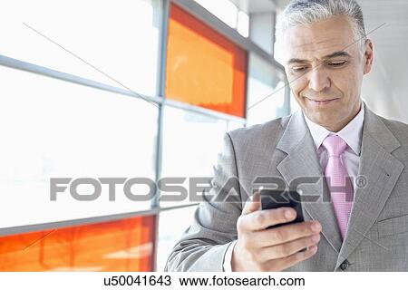 Stock Image - Middle aged businessman using cell phone at railroad station. Fotosearch