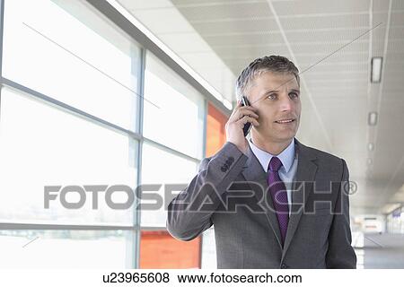 Stock Photo - Middle aged businessman using mobile phone at train station. Fotosearch