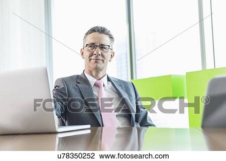 Middle-aged businessman with laptop sitting at conference table View Large Photo Image Stock Image - Middle-aged businessman with laptop sitting at conference table. Fotosearch