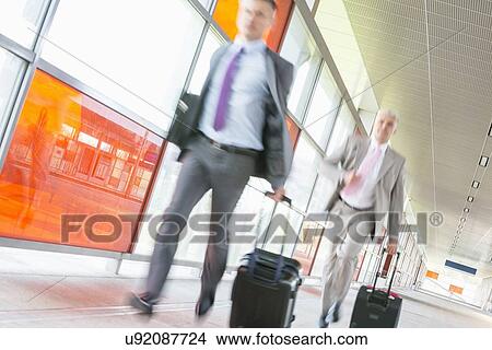 Picture - Middle aged businessmen with luggage rushing on railroad platform. Fotosearch
