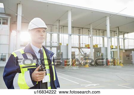 Middle-aged male worker holding walkie-talkie while looking away in shipping yard View Large Photo Image Stock Image - Middle-aged male worker holding walkie-talkie while looking away in shipping yard. Fotosearch