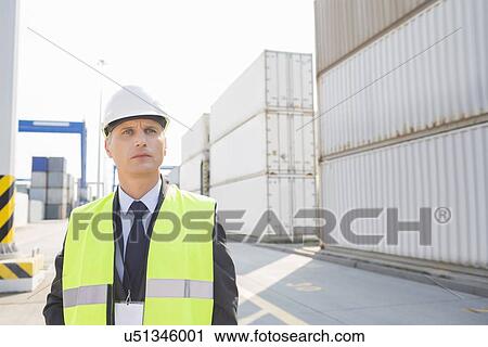 Stock Image - Middle-aged male worker looking away in shipping yard. Fotosearch