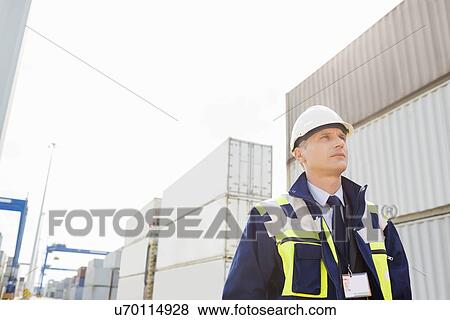 Middle-aged male worker looking away in shipping yard View Large Photo Image Stock Photo - Middle-aged male worker looking away in shipping yard. Fotosearch