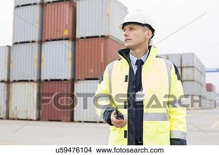 Middle-aged man holding walkie-talkie in shipping yard View Large Photo Image Picture - Middle-aged man holding walkie-talkie in shipping yard. Fotosearch