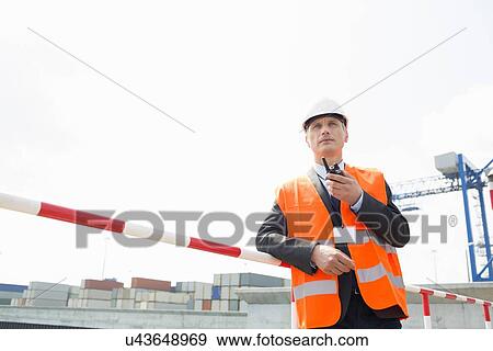 Stock Photo - Middle-aged man using walkie-talkie in shipping yard. Fotosearch