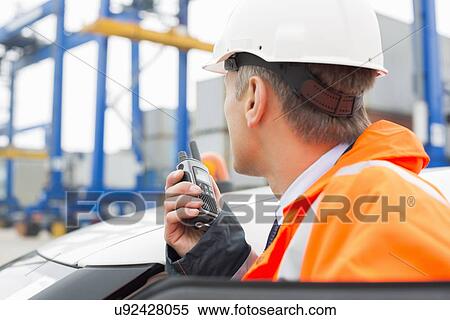 Middle-aged man using walkie-talkie while standing beside car in shipping yard View Large Photo Image Stock Photography - Middle-aged man using walkie-talkie while standing beside car in shipping yard. Fotosearch