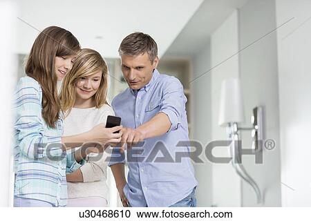 Middle-aged man with daughters using smart phone at home View Large Photo Image Stock Image - Middle-aged man with daughters using smart phone at home. Fotosearch