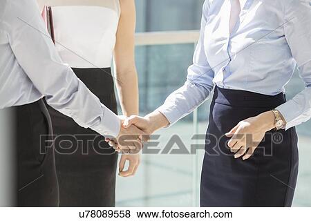 Midsection of businesswomen shaking hands in office View Large Photo Image Stock Photo - Midsection of businesswomen shaking hands in office. Fotosearch