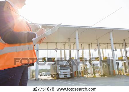 Midsection of female worker writing on clipboard while looking at truck entering in shipping yard View Large Photo Image Stock Photo - Midsection of female worker writing on clipboard while looking at truck entering in shipping yard. Fotosearch