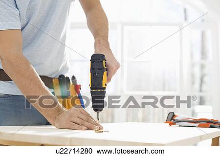 Stock Image - Midsection of man drilling nail on table. Fotosearch