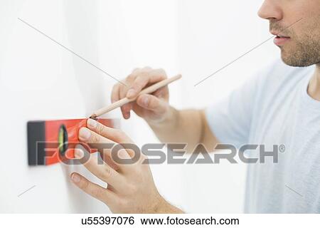 Stock Photograph - Midsection of man marking on wall with level. Fotosearch
