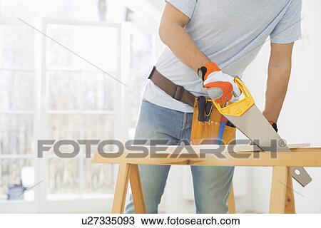 Stock Image - Midsection of man sawing wood in new house. Fotosearch