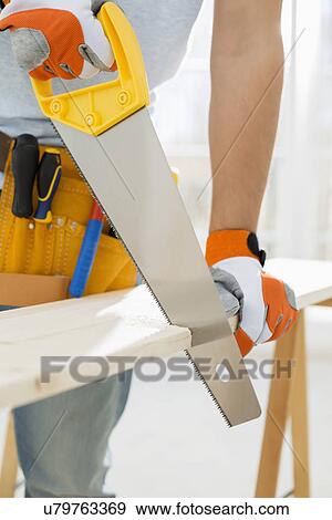 Stock Photo - Midsection of man sawing wood in new house. Fotosearch