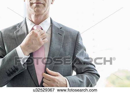 Midsection of mature businessman adjusting necktie View Large Photo Image Stock Photo - Midsection of mature businessman adjusting necktie. Fotosearch