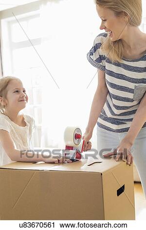 Mother and daughter looking at each other while packing cardboard box at home View Large Photo Image Stock Image - Mother and daughter looking at each other while packing cardboard box at home. Fotosearch