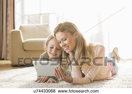 Stock Photo - Mother and daughter using digital tablet on floor at home. Fotosearch