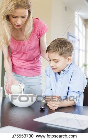 Stock Image - Mother pouring milk for son at table. Fotosearch