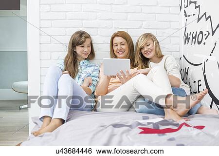 Mother with daughters using tablet PC in bedroom View Large Photo Image Stock Photograph - Mother with daughters using tablet PC in bedroom. Fotosearch