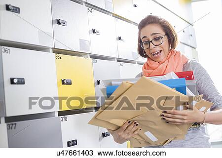 Stock Image - Overworked businesswoman holding documents in locker room at creative office. Fotosearch