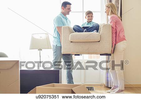 Parents carrying son on armchair in new house View Large Photo Image Stock Image - Parents carrying son on armchair in new house. Fotosearch