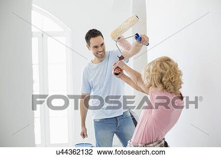 Stock Image - Playful couple fighting while painting new house. Fotosearch