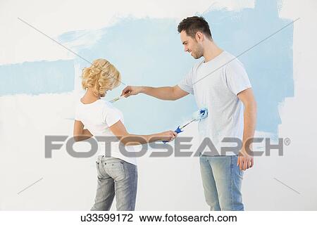 Stock Image - Playful couple painting each other in new house. Fotosearch