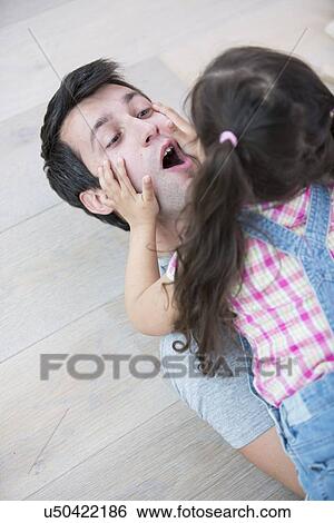 Playful daughter on top of father at home View Large Photo Image Stock Photograph - Playful daughter on top of father at home. Fotosearch