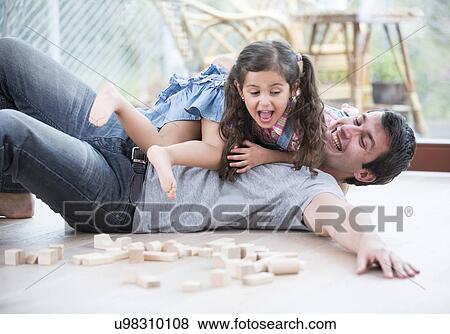 Playful daughters on top of father at home View Large Photo Image Stock Photo - Playful daughters on top of father at home. Fotosearch